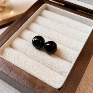 Primer plano de elegantes pendientes de perlas negras en un joyero de madera vintage