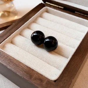 Primer plano macro detallado de pendientes de bola negros minimalistas en caja de madera