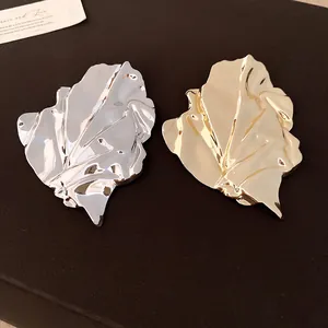 Detailed view of metallic gold and silver irregular wrinkled leaf brooches with high gloss finish.