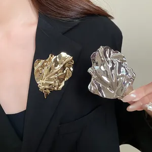Detailed view of elegant irregular pleated metal leaf brooches in gold and silver