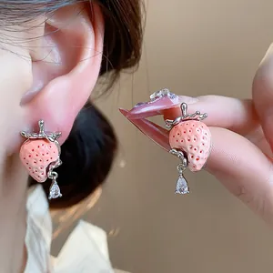 Dettaglio di orecchini a lobo a fragola in resina rosa con goccia di zircone lucido.