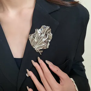 Close-up detail of a minimalist silver metallic leaf brooch with wrinkled texture