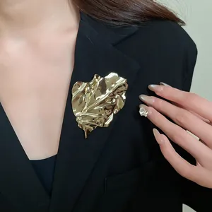 Detail view of a gold irregular pleated leaf brooch worn on a professional black blazer