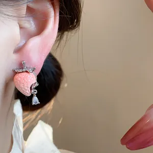 Macro dettaglio di un orecchino a fragola in resina rosa con una goccia pendente di zircone chiaro