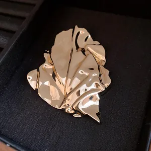 Macro detail of a high-end gold metal irregular wrinkled leaf brooch with shine