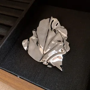 Detailed view of the metallic irregular pleated leaf brooch with a high-shine finish