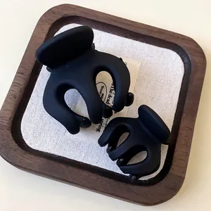 Pair of minimalist matte black wavy hair claw clips presented on a decorative wooden tray