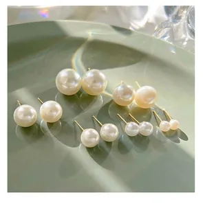 Detail view showing various sizes of glossy white pearl stud earrings on a green plate
