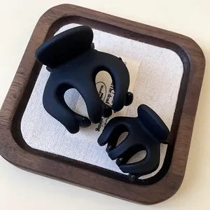 Close-up of matte black wave-shaped hair claw clips in two sizes on a wooden tray