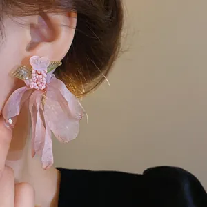 Dettaglio ravvicinato di orecchini a fiore in tulle rosa con perline e foglie verdi.