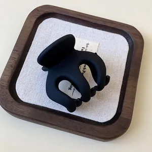 Close-up detail of a matte black wave hair claw clip presented on a wooden display tray