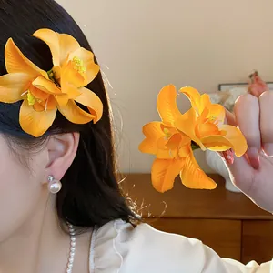 Gros plan de barrettes à fleurs en tissu orange portées sur les cheveux et tenues en main.