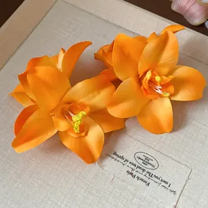 Vue détaillée de deux pinces à cheveux en fleurs de tissu orange sur un support en lin.