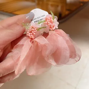 Primo piano di orecchini a fiore in rete rosa con ago in argento e dettagli in perline.