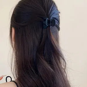 Detailed view of a minimalist matte black hair claw clip on long wavy brown hair