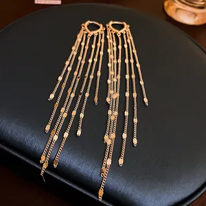 Close-up of gold-tone tassel earrings with delicate chains and heart-shaped hoops.