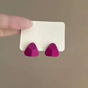 Detail view of matte magenta triangle stud earrings featuring a 3D faceted geometric design