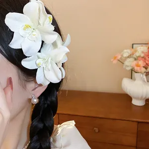 Détail d'une pince à cheveux fleur artificielle en tissu blanc sur une tresse foncée