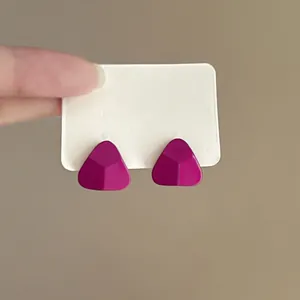 Detail view of vibrant magenta minimalist triangle stud earrings on a white card
