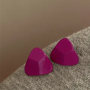 Close-up detail of minimalist purple triangular geometric stud earrings on gray fabric texture