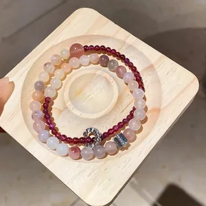 Detailed view of layered beaded bracelets featuring flower charms and garnet beads on wood