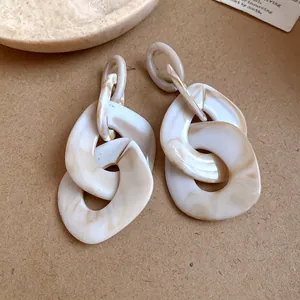 Detailed close-up of oversized geometric acrylic chain link earrings with cream marble texture
