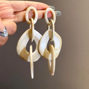 Close-up view of chunky acrylic geometric chain earrings featuring a cream marbled pattern