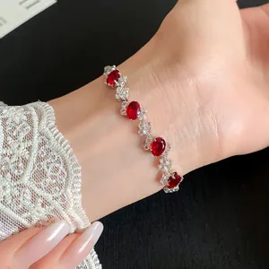 Close-up of an elegant bracelet featuring red oval zircons on a lace-sleeved wrist detail