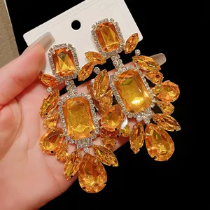 Close-up detail of oversized retro earrings with orange faceted crystals and rhinestones