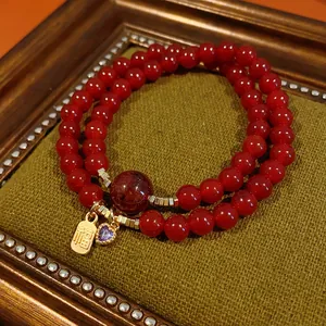 Close-up of a double-strand red beaded bracelet with a gold Fu charm and purple heart.