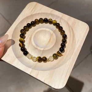 Detailed view of natural tiger eye and yellow crystal beaded bracelet on a wood stand