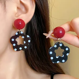 Close-up of retro red stud and black polka dot flower dangle earrings on a model