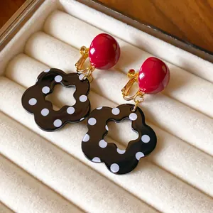 Close-up of retro flower earrings with polka dots and red stud in a beige jewelry box.