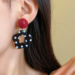 Macro detail of retro black polka dot hollow flower earrings with red stud on model