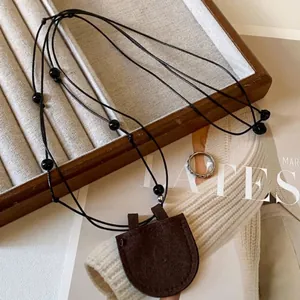 Detailed macro view of dark brown leather pouch pendant on a black beaded necklace cord
