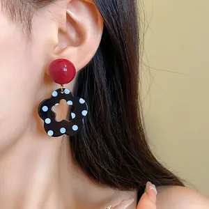Detail view of retro red and black polka dot flower drop earrings on model