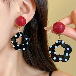 Macro view of retro hollow flower earrings with black and white polka dots and red studs.