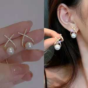 Detailed close-up of elegant gold 'X' cross diamond earrings with white pearls