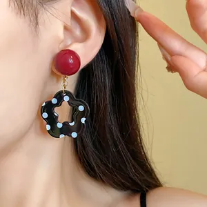 Close-up of retro hollow flower earrings with white polka dots and red round studs.