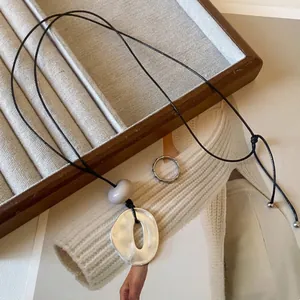Close-up view of a geometric silver pendant on a black leather cord over a magazine.