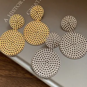 Detailed close-up showing gold and silver hollow mesh circular pendant earrings on a book background