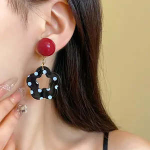 A close-up view of retro black polka dot flower dangle earrings with a red stud on a model