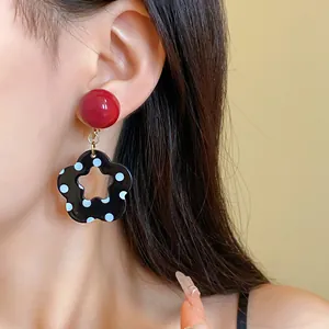 Detail of vintage earrings with red round studs and black floral pendants featuring white polka dots.