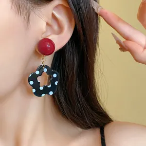 Detailed close-up of retro black flower polka dot earrings with red stud on model's ear