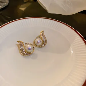 Close-up of elegant gold fish-tail earrings with pavé crystals and pearl.