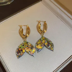 Close-up of golden twisted hoop earrings with colorful glittery mermaid tail charms