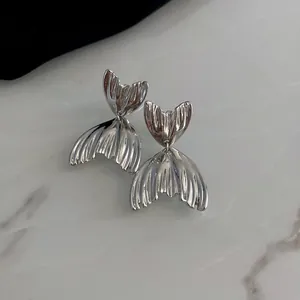 Detailed view of silver-toned fishtail earrings with a ribbed metallic texture on marble.