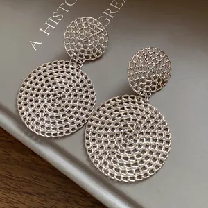 Close-up detail of silver hollow circular drop earrings with intricate woven mesh texture