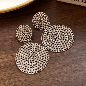 Close-up of golden hollow round mesh drop earrings on a dark wood surface