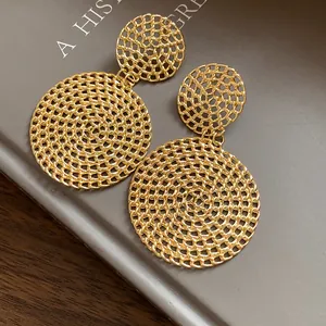 Close-up of elegant gold-toned hollow mesh circular drop earrings on a gray background